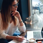 Young And Smart. Beautiful Young Woman Work In Caffe. Woman Writing And Using Laptop While Sitting I